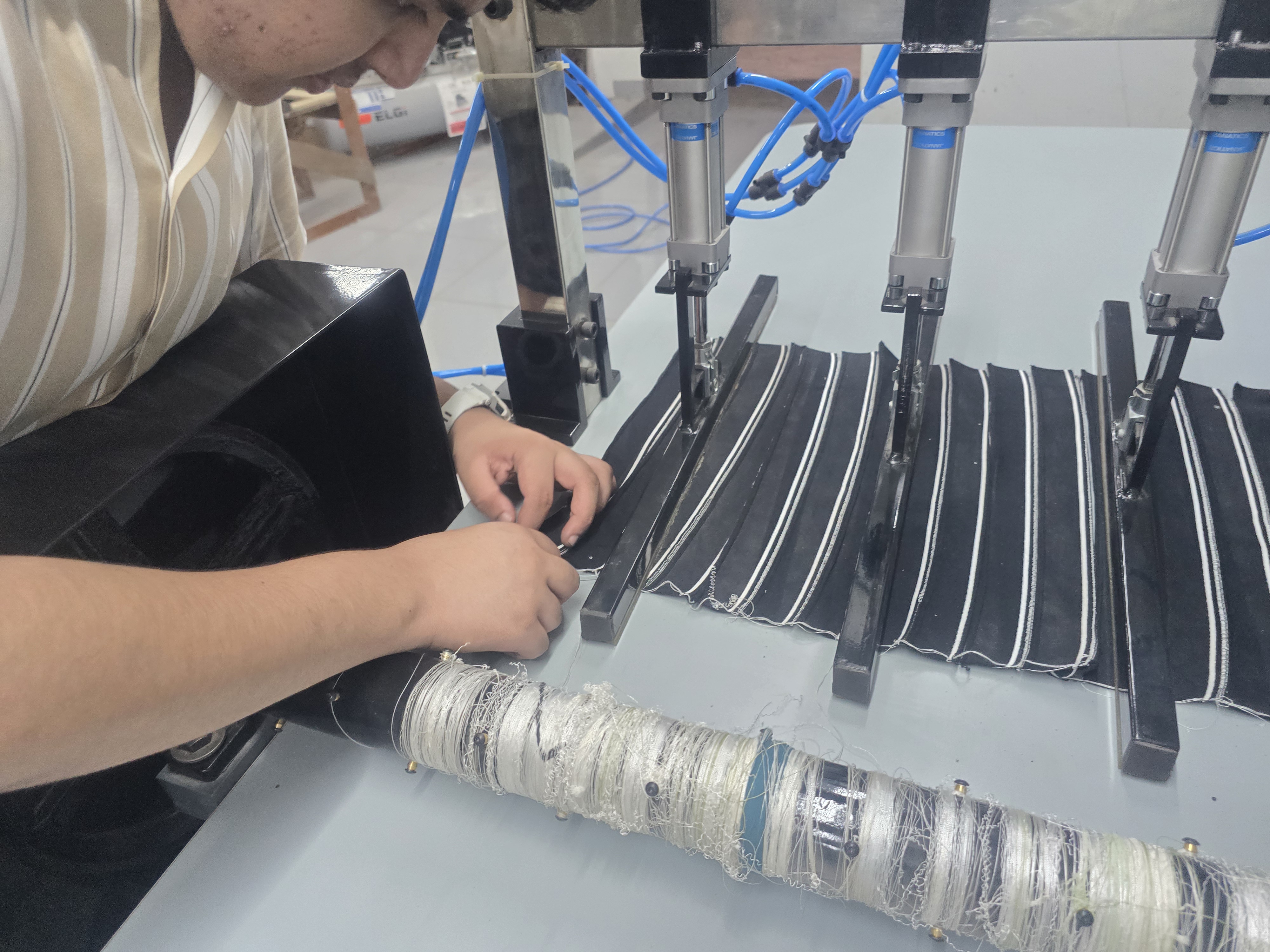 Hands adjusting actuators over striped flat-knit fabric rolls